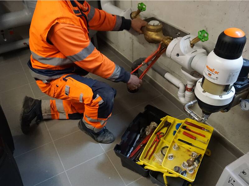 Monteur arbeite mit der Rohrzange an einem Wasserzähler im Keller eines Gebäudes